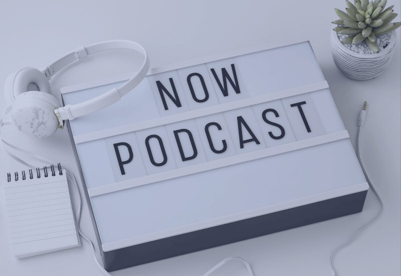Lichtkasten mit Aufschrift Now Podcast, Kopfhörer und Block